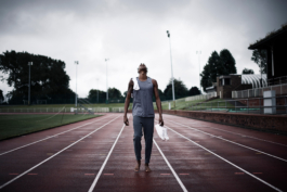 Man on running track holding trainers in his left hand with socks on his right shoulder, looking up towards the sky. Wearing Castore clothing. Ross Woodhall - Action & Lifestyle Photography