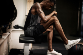 man in gym, resting on a bench with foot on weighted ball, with weighs behind. Ross Woodhall - Action & Lifestyle Photography
