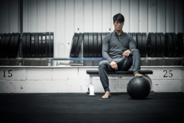 Man in gym, relaxing on bench, weights in background, resting on foot on weighted ball. Ross Woodhall - Action & Lifestyle Photography