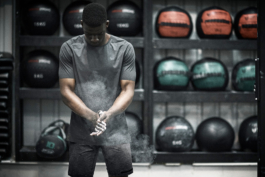 man in gym with exercise equipment behind, rubbing hands together with chalk. wearing Castore. Ross Woodhall - Action & Lifestyle Photography