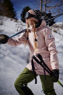 female skier with her hair in plaits, holding her skis over her shoulder with googles and woolly hat on. Ross Woodhall - Action & Lifestyle Photography