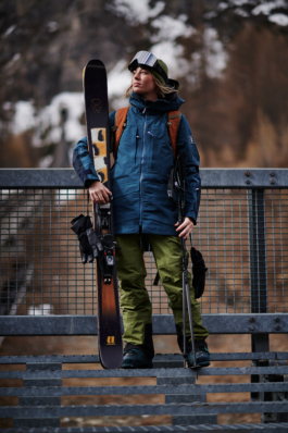 female skier standing on some steel stairs holding her skis and poles and looking out. Ross Woodhall - Action & Lifestyle Photography