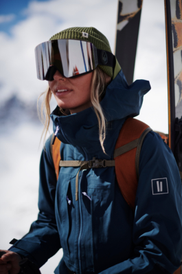 close up of female skier with skis strapped to her backpack wearing a woolly hat with googles on. Ross Woodhall - Action & Lifestyle Photography