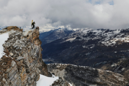 man with ski's strapped to his backpack looking over out over a cliff at the mountains in the distance. Ross Woodhall - Action & Lifestyle Photography