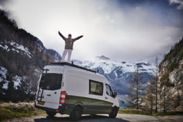woman stood on top of her camper van with arms out stretched, with mountains in the background. Ross Woodhall - Action & Lifestyle Photography
