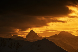 Mountain peaks in the distance shot at sunset with an amazing orange colour and dark clouds. Ross Woodhall - Action & Lifestyle Photography