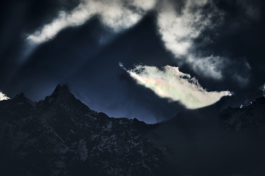 Moody snowy mountain range with clouds with bright sun beams on to the distant mountain. casting a mountain peak shadow into the sky. Ross Woodhall - Action & Lifestyle Photography