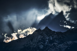 Moody snowy mountain range with clouds with bright sun beams on to the distant mountain. casting a mountain peak shadow into the sky. Ross Woodhall - Action & Lifestyle Photography