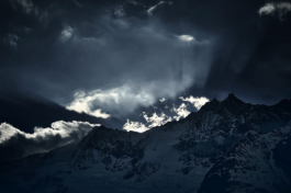 Moody black and white snowy mountain range with clouds with bright sun beams on to the distant mountain. Ross Woodhall - Action & Lifestyle Photography