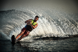 Waterskier holding the line mid turn with large water rooster behind him. Wearing shorts and life vest on a mono water ski. Ross Woodhall - Action & Lifestyle Photography