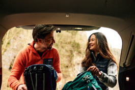 A couple, man and woman at the back of the car getting their backpacks ready for the days hiking/walking. Smiling and looking at each other from the open boot of their car. Ross Woodhall - Action & Lifestyle Photography