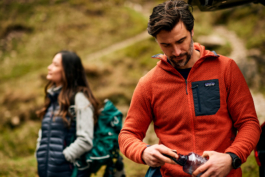 A couple, man and woman out hiking/walking for the day. Having a break and taking in the view. Man is shutting the lid to his water bottle facing camera, woman is looking out in the distance. Ross Woodhall - Action & Lifestyle Photography