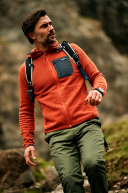 Man walking downhill, wearing Patagonia orange fleece, green trousers and a small backpack, looking out into the distance towards his left. Ross Woodhall - Action & Lifestyle Photography