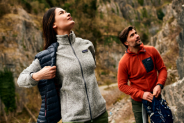 A couple, a man and a woman wearing Patagonia clothing looking up towards what could be a climbing route. Lad has a gilet jacket half off. Ross Woodhall - Action & Lifestyle Photography