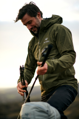 A man holding some walking poles, getting ready to put them away into his backpack which is just in the foreground. Man is wearing a green Arc.teryx jacket. Ross Woodhall - Action & Lifestyle Photography