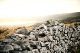 Image of a stone wall in the hills, above a lake which is reflecting the sunshine. Ross Woodhall - Action & Lifestyle Photography