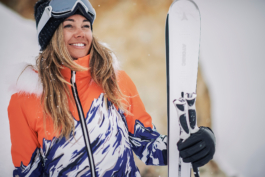 female skier with long hair, holding pair of skis. Ross Woodhall - Action & Lifestyle Photography