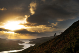 Male fell runner, running up a hill side with river estuary below. with sun setting behind some clouds. Ross Woodhall - Action & Lifestyle Photography