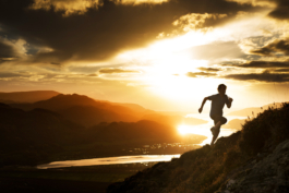 Man fell running up a hill side with the sunsetting behind with the orange glow reflected in the water of the estuary. Ross Woodhall - Action & Lifestyle Photography