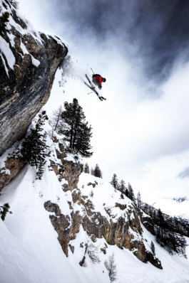 Skier dropping from a rocky cliff with trees. Photographed from below, looking up to skier with his ski's slightly crossed. Ross Woodhall - Action & Lifestyle Photography