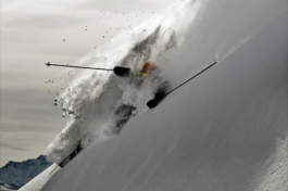 A solo skier coming down a steep slope off piste. Snow thrown into the air & covering the skier. Only seeing both poles & part of his helmet & a ski. Ross Woodhall - Action & Lifestyle Photography