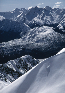 Shot of a solo skier coming down the edge of a mountain in New Zealand with far reaching views of the snowy mountains in the background. Ross Woodhall - Action & Lifestyle Photography