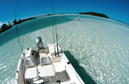 Fish eye image of a Man up to his thighs in crystal clear sea water in the Caribbean fly fishing taken from small fishing motor yacht anchored further out with fishing rods placed ready to go with a small island in the background. Ross Woodhall - Action & Lifestyle Photography