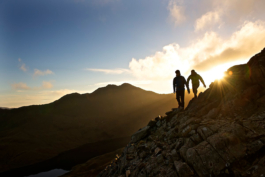 two men out hiking on a rocky ridge line, walking down with sun setting behind them. Ross Woodhall - Action & Lifestyle Photography