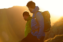 two men out hiking looking down, away from camera, with hiking jacket and backpack on, in the sunset. Ross Woodhall - Action & Lifestyle Photography