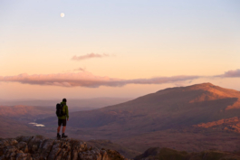 single man out hiking. Pausing to take in view at sunset of hills and a lake in the valley. Ross Woodhall - Action & Lifestyle Photography