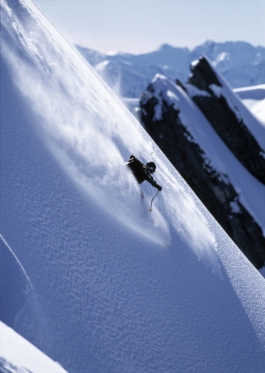 Image of Kent Kreitler skiing down a mountain with the mountains in the background & light flurries of snow around him. Ross Woodhall - Action & Lifestyle Photography