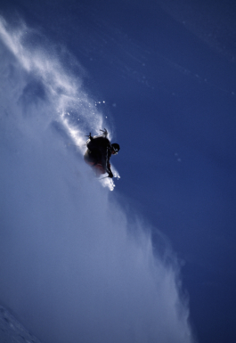 Solo skier Kent Kreitier coming down off piste on the mountain caught in a line of sunlight with snow flurries behind him, caught in the wind. Ross Woodhall - Action & Lifestyle Photography