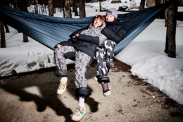 two skiers chilling in a hammock, surrounded by trees and snow. Ross Woodhall - Action & Lifestyle Photography