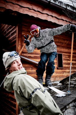 two skiers being playful in their poses towards the camera. In front of a wooden chalet. Ross Woodhall - Action & Lifestyle Photography
