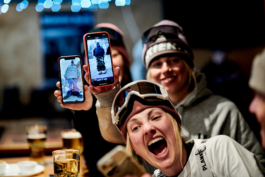Skiers at apres ski with a few beers showing themselves in their ski gear on their phones towards the camera Ross Woodhall - Action & Lifestyle Photography