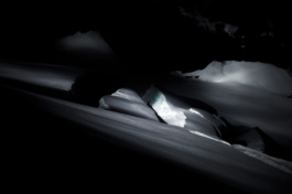 Black and white image, moody image of crack in snow with a shaft of light. Ross Woodhall - Action & Lifestyle Photography