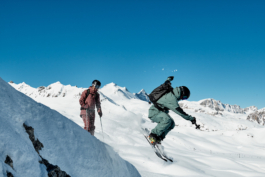 two skiers with one launching off the mountain and caught mid air with the other looking on. Ross Woodhall - Action & Lifestyle Photography