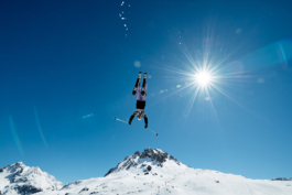 Skier mid air, mid somersault. Shot towards the sun with the mountain in the background. Ross Woodhall - Action & Lifestyle Photography