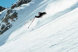 Skier mid turn with pole outstretched, off piste with rocks in background and snow in foreground. Ross Woodhall - Action & Lifestyle Photography
