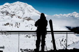 Skier in the shadow with skis looking out on to the mountain and ski runs with clouds over the valley. Ross Woodhall - Action & Lifestyle Photography