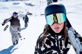 three skiers hiking up the hill, close up of first woman playfully sticking her tongue out towards the camera. Ross Woodhall - Action & Lifestyle Photography