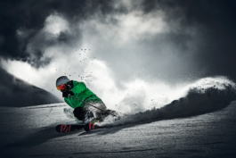 Solo skier off piste with bright green jacket on, turning with snow flicked up, image is saturated to black and white. Ross Woodhall - Action & Lifestyle Photography