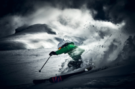 Solo skier with bright green jacket on, skiing off piste with snow flicked up behind them. Ross Woodhall - Action & Lifestyle Photography