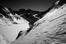 Black and white image of a solo skier, off piste, above a frozen covered lake. Ross Woodhall - Action & Lifestyle Photography