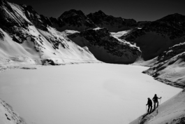 black and white image of two skiers stopped above a frozen covered lake, off piste. Ross Woodhall - Action & Lifestyle Photography