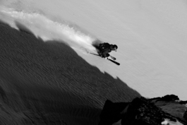 Black and white image of a solo sjier out of the shadow of the mountain, skiing down, off piste. Ross Woodhall - Action & Lifestyle Photography