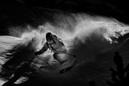 Black and white image of a skier with snow particles swirling behind them. Ross Woodhall - Action & Lifestyle Photography