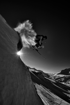 Black and white image of a skier jumping off piste with a glimpse of the sun. Ross Woodhall - Action & Lifestyle Photography