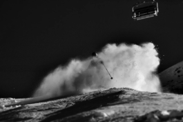 Black and white image of skier under a chairlift, surrounded by particles of snow. Ross Woodhall - Action & Lifestyle Photography