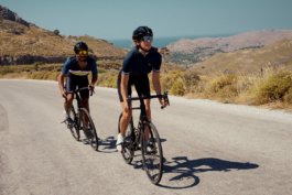 A couple on road bikes climbing a gentle hill on a tarmac road with the valley and sea in the background. Ross Woodhall - Action & Lifestyle Photography